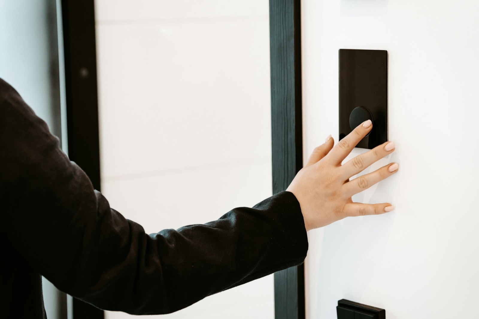 A hand pressing an access panel beside a door