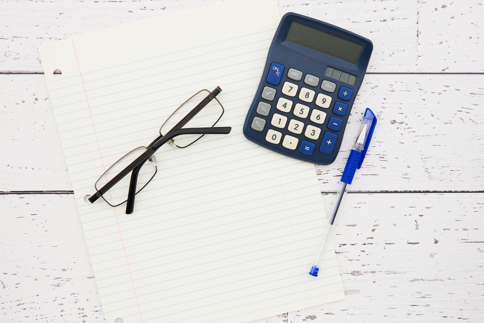 A calculator, reading glasses and a pen beside a sheet of paper